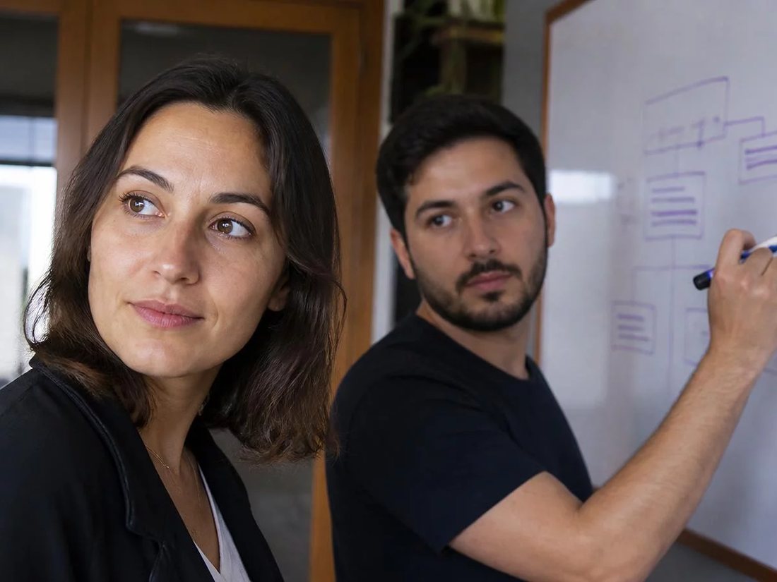 Duas pessoas diante do quadro branco com a armação de um argumento rabiscada